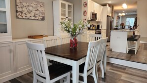 Une cuisine moderne avec des meubles blancs, un îlot central doté de tabourets de bar et un vase rempli de fleurs sur la table à manger.