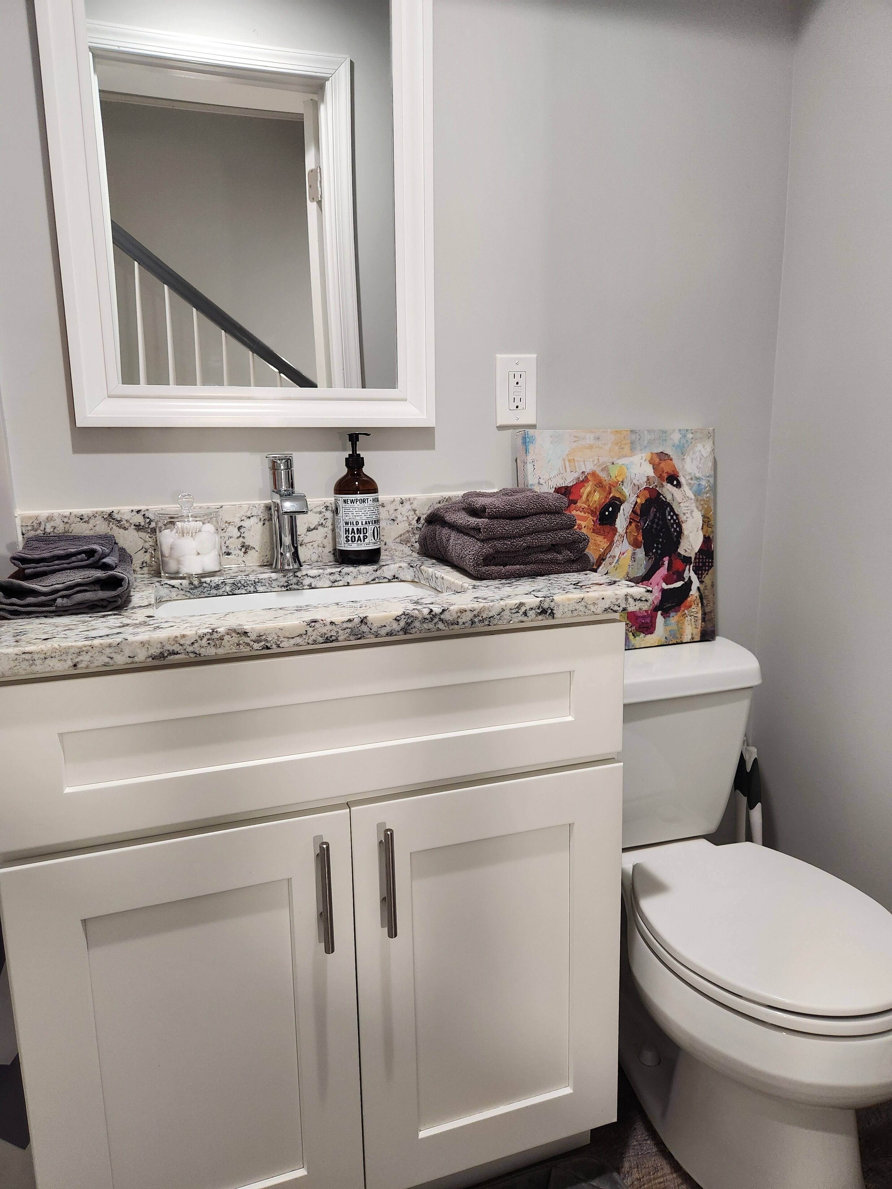 Une salle de bain avec un lavabo blanc, un miroir, des toilettes et une œuvre d’art colorée accrochée au mur.