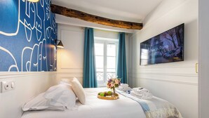 A hotel room with a bed, a TV on the wall, a window with curtains, and a bedside table with a plant. - Charming Studio - 2P - Pigalle/sacre-coeur (Paris)