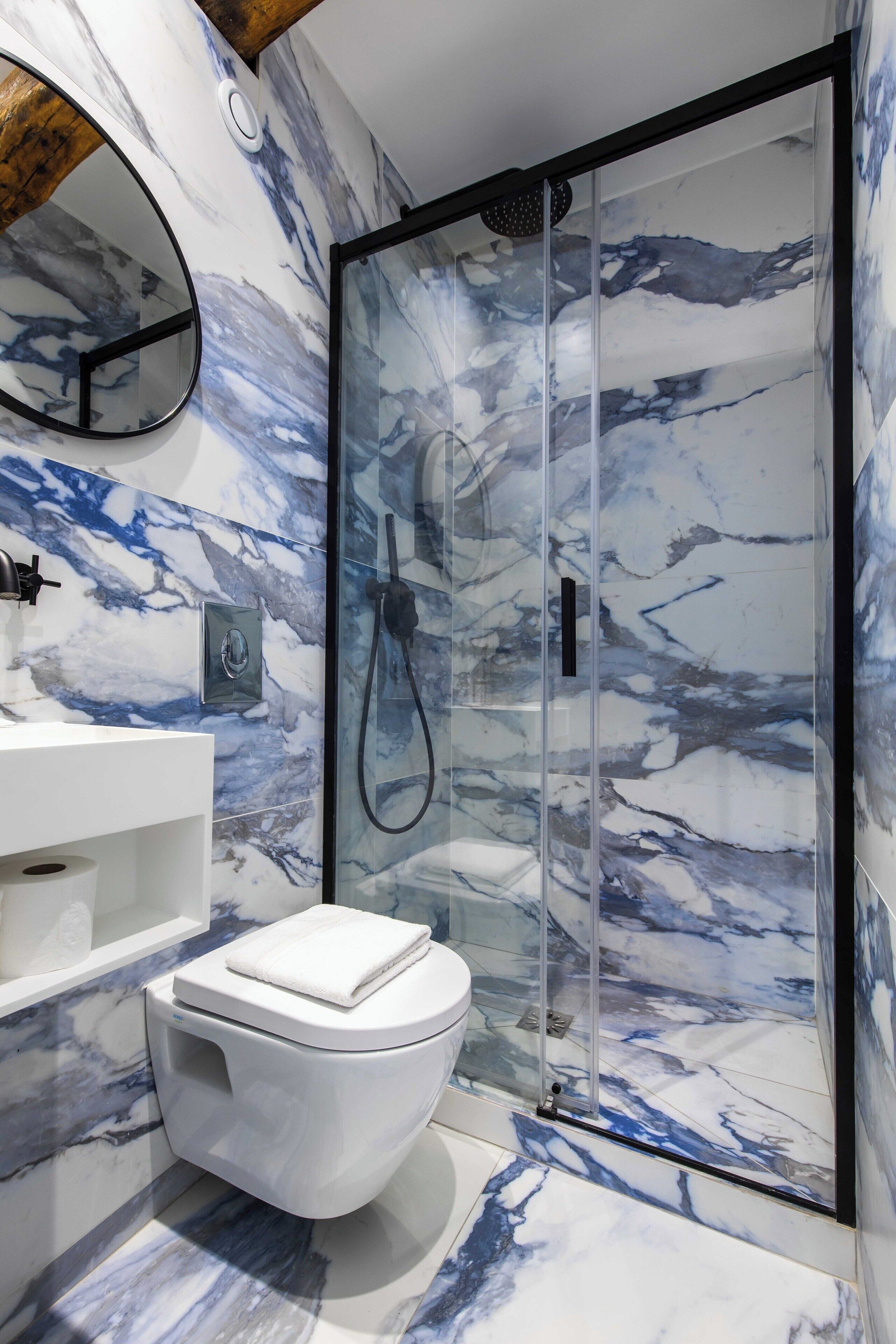 A bathroom with a marble backsplash, a toilet, a sink, and a glass-enclosed shower.