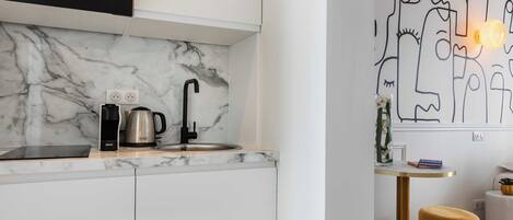 A modern kitchen with white cabinetry, a marble backsplash, and a black microwave.