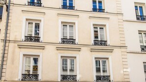 Egy többszintes épület, klasszikus építészeti stílusban, szimmetrikus homlokzattal, egyenletesen elhelyezett ablakokkal és díszes, kovácsoltvas korlátokkal a balkonokon.