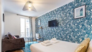 Un dormitorio con una cama, un sofá, un televisor y un papel tapiz estampado.