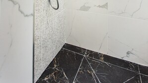 Un baño con ducha, baldosas blancas con motas y suelo de mármol negro.