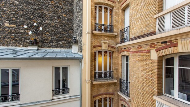 Un edificio de varios pisos con fachada de ladrillo, múltiples balcones con barandillas de hierro forjado y ventanas grandes.
