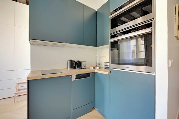 Eine kompakte Küche mit blauen Schränken, einem integrierten Geschirrspüler und einem Edelstahlbackofen.