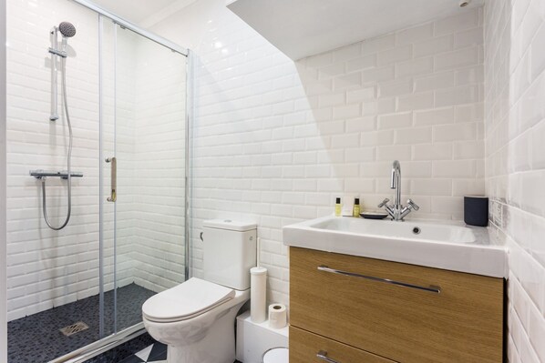 A modern bathroom with a glass shower enclosure, a white toilet, and a wooden vanity with a sink.
