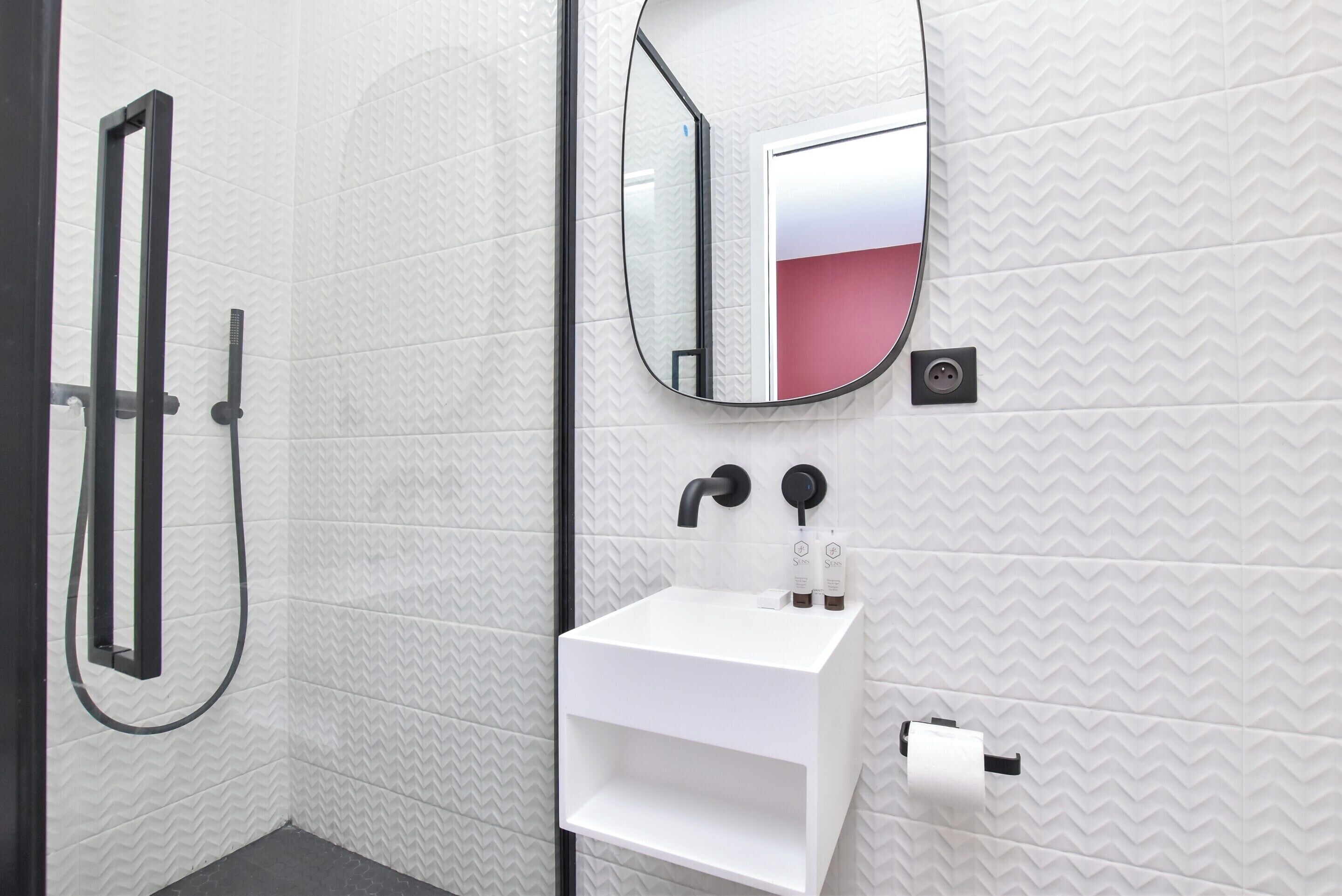 Une salle de bain moderne équipée d’une douche, d’un lavabo avec miroir et d’articles de toilette.
