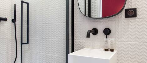 A modern bathroom with a glass shower enclosure, a white sink with a black faucet, and a mirror with a red accent.