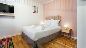 Una habitación de hotel con una cama, un televisor en la pared, una mesita de noche con lámpara y una alfombra colorida en el suelo.