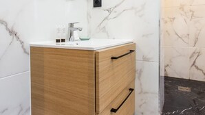 Un baño con pared de mármol, tocador de madera, espejo redondo y piso con estampado blanco y negro.
