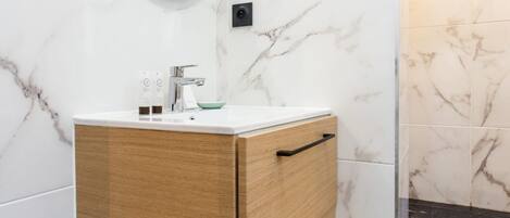 A bathroom with a marble wall, a wooden vanity, a round mirror, and a black and white patterned floor.