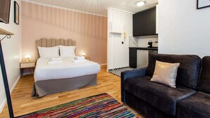 Un dormitorio moderno con cama, mesitas de noche, un sofá y una cocina al fondo.