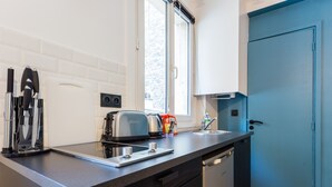 A modern kitchen with a black countertop, a toaster, a kettle, and a coffee machine. There is a window providing natural light and a blue door. - Cozy Studio in the Heart of Paris (Paris)