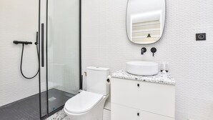 A modern bathroom with a glass shower enclosure, a white toilet, a marble countertop, and a wall-mounted oval mirror. - Intimate Studio - 2P - Beaugrenelle/tour Eiffel (Paris)