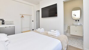 A hotel room with a bed, a TV mounted on the wall, a bathroom with a sink and mirror, and a small desk with a coffee maker. - Intimate Studio - 2P - Beaugrenelle/tour Eiffel (Paris)