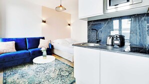 Una sala de estar moderna con un sofá azul, una cama blanca y una zona de cocina con microondas y cafetera.