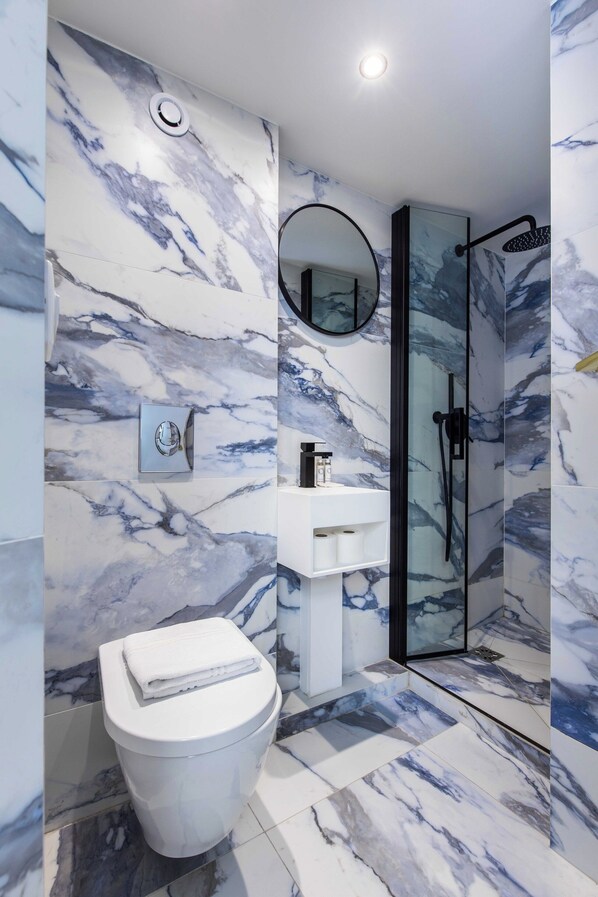 A bathroom with marble walls, a toilet, a sink, and a glass-enclosed shower. - Modern Studio - 2P - Pigalle/sacre-coeur (Paris)