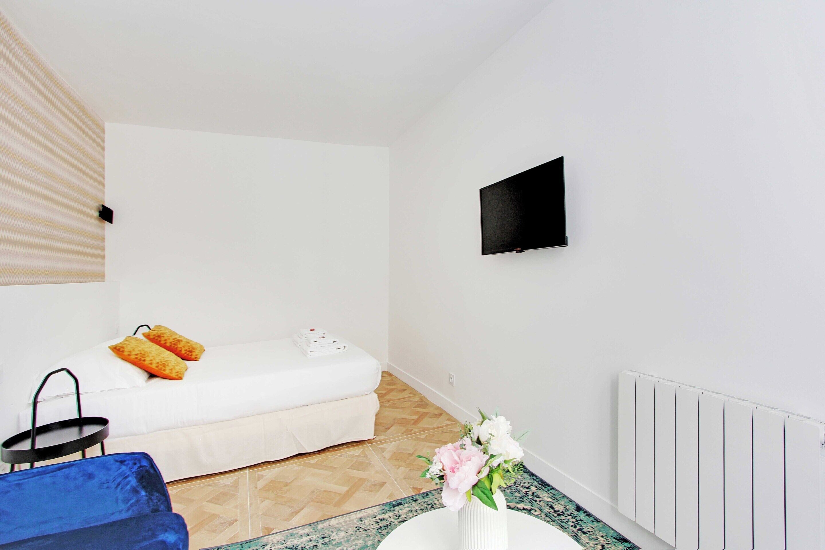 A small, clean room with a bed, a TV mounted on the wall, and a radiator.