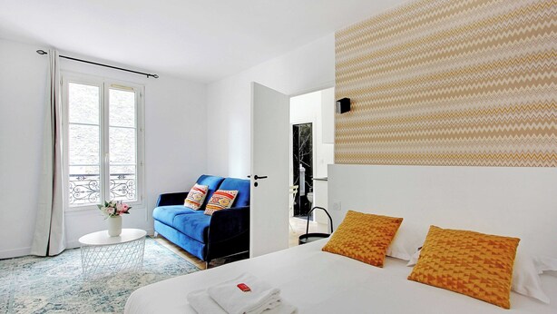 Habitación de hotel con cama, sofá azul, una mesita redonda y pared estampada.