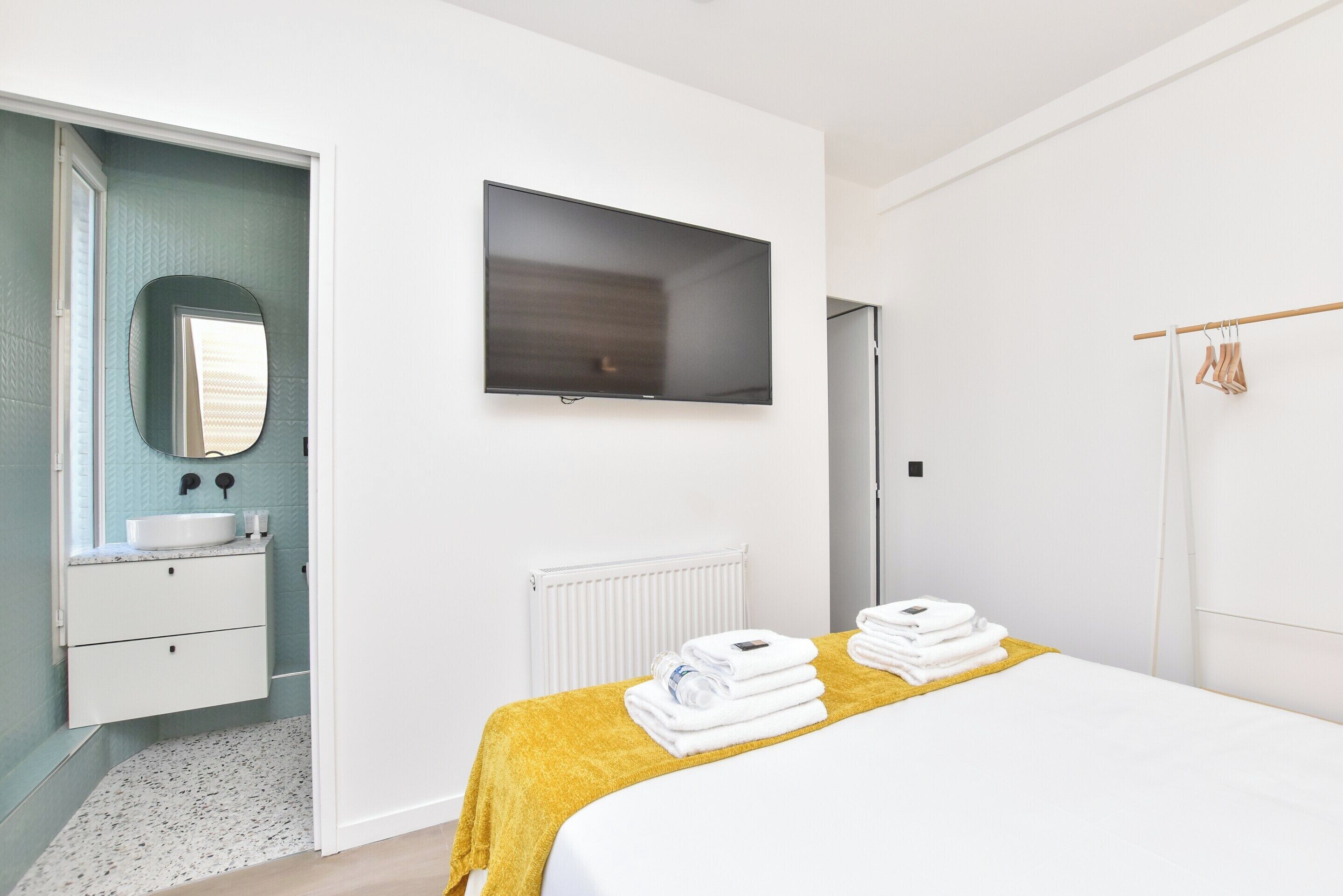 Een moderne hotelkamer met een bed, een televisie, een badkamer met een wastafel en spiegel, en een handdoekrek.