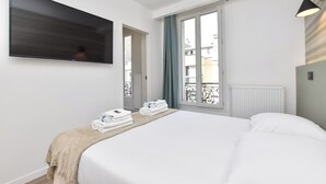 A hotel room with a large bed, a flat-screen TV mounted on the wall, a window with a view of the city, and a radiator. - Charming Studio - 2P- Javel/tour Eiffel (Paris)