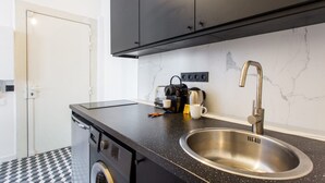 Cuina compacta amb taulell negre, rentamiques d'acer inoxidable i una cafetera.