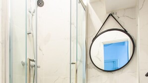 Un bany modern amb dutxa d'envidrierament, sòl de marbre i un penjall de fusta amb un mirall rodó.