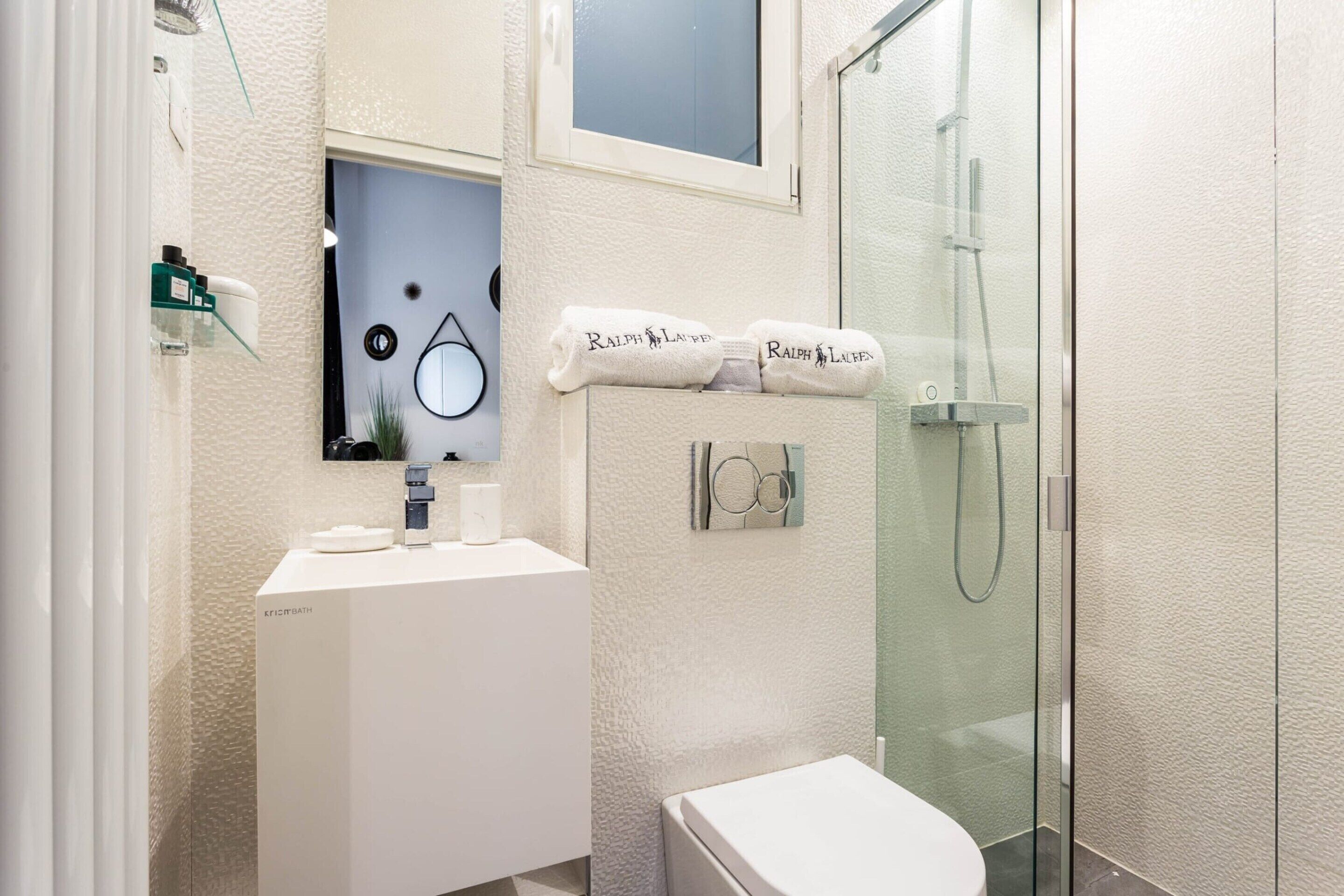 Une salle de bain moderne avec un lavabo blanc, un miroir et une cabine de douche en verre.