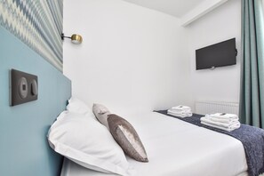 Une chambre d’hôtel équipée d’un lit, d’oreillers, d’un téléviseur à écran plat et d’un luminaire fixé au mur.