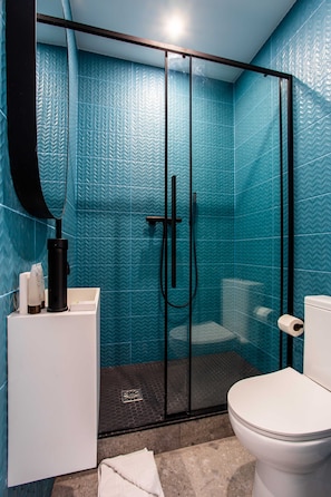 Une salle de bain avec une douche à parois de verre, des toilettes blanches et un lavabo doté d’un robinet noir.