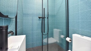 Ein Badezimmer mit blauen, gemusterten Fliesen, einer Glasdusche, einem weißen Waschbecken und einer Toilette.