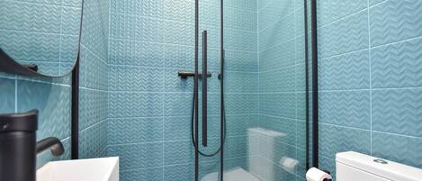 Un baño con baldosas azules estampadas, cabina de ducha de vidrio, lavamanos blanco y un inodoro.