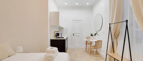 A hotel room with a bed, a small kitchenette, a dining area, and a bathroom.