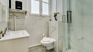 Egy modern fürőszoba üveg válaszfallal ellátott zuhanyzóval, WC-vel és mosdókagylóval.