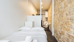 A hotel room with a bed, white linens, a stone wall, and a chair.