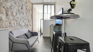 A modern kitchen with a stone wall, a grey sofa, and a black stool.