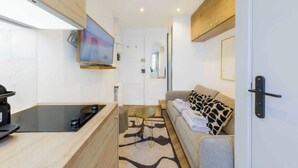 A compact living space with a kitchenette, a sofa with patterned cushions, and a flat-screen TV mounted on the wall. - Appartement in the Heart of Paris Eiffel Tower (Paris)