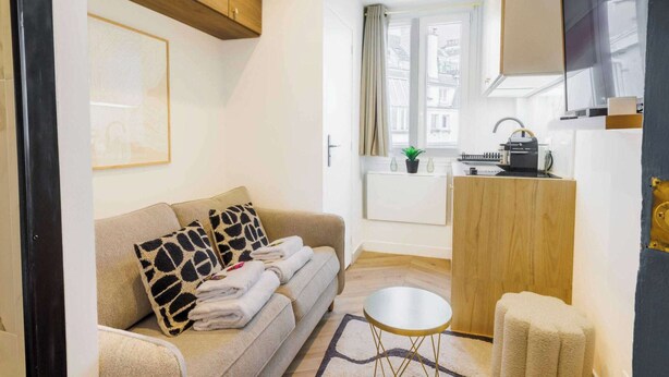 A modern living room with a sofa, a small round table, and a kitchen area with a sink and countertop. - Appartement in the Heart of Paris Eiffel Tower (Paris)
