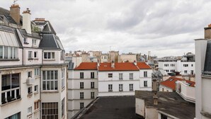A view of a residential area with multiple buildings, including a white building with a red roof and a grey building with a sloped roof. - Appartement in the Heart of Paris Eiffel Tower (Paris)
