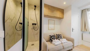 A modern bathroom with a glass-enclosed shower, a beige sofa with patterned cushions, and a wooden cabinet above the sofa. - Appartement in the Heart of Paris Eiffel Tower (Paris)