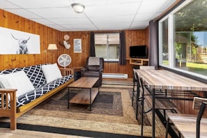 Et værelse med sofa, stol, bord, ventilator og fjernsyn.