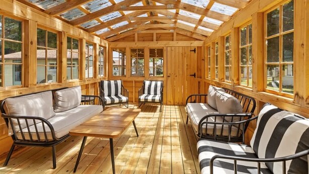 A sunroom with wooden walls and a glass ceiling, furnished with sofas and chairs.