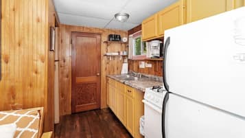 Una cocina compacta con paredes de madera, un refrigerador blanco, una estufa y un lavamanos.