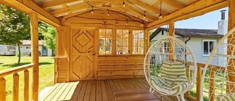 A wooden porch with a covered roof, a hanging chair, and a view of a house in the background.