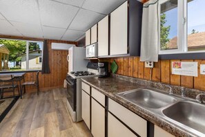 Una cocina compacta con armarios de madera, estufa a gas, microondas y pileta doble.