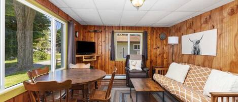 A cozy cabin interior with a wooden dining table, chairs, a sofa, and a television.