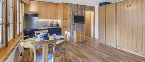 Une cuisine moderne avec des meubles en bois, une table à manger avec des chaises et un téléviseur fixé au mur.