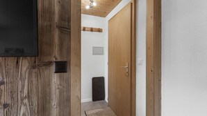 A hallway with a wooden door, a small rug, and a ceiling light fixture. - Cosy studio with breathtaking view (Saint-Luc)
