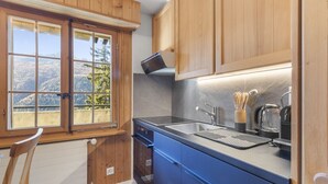 A kitchen with wooden cabinets, a built-in oven, a sink, and a window overlooking a mountainous landscape. - Cosy studio with breathtaking view (Saint-Luc)